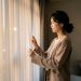 Une actrice coréenne pensive ferme doucement des rideaux dans un intérieur contemporain baigné de lumière chaleureuse.